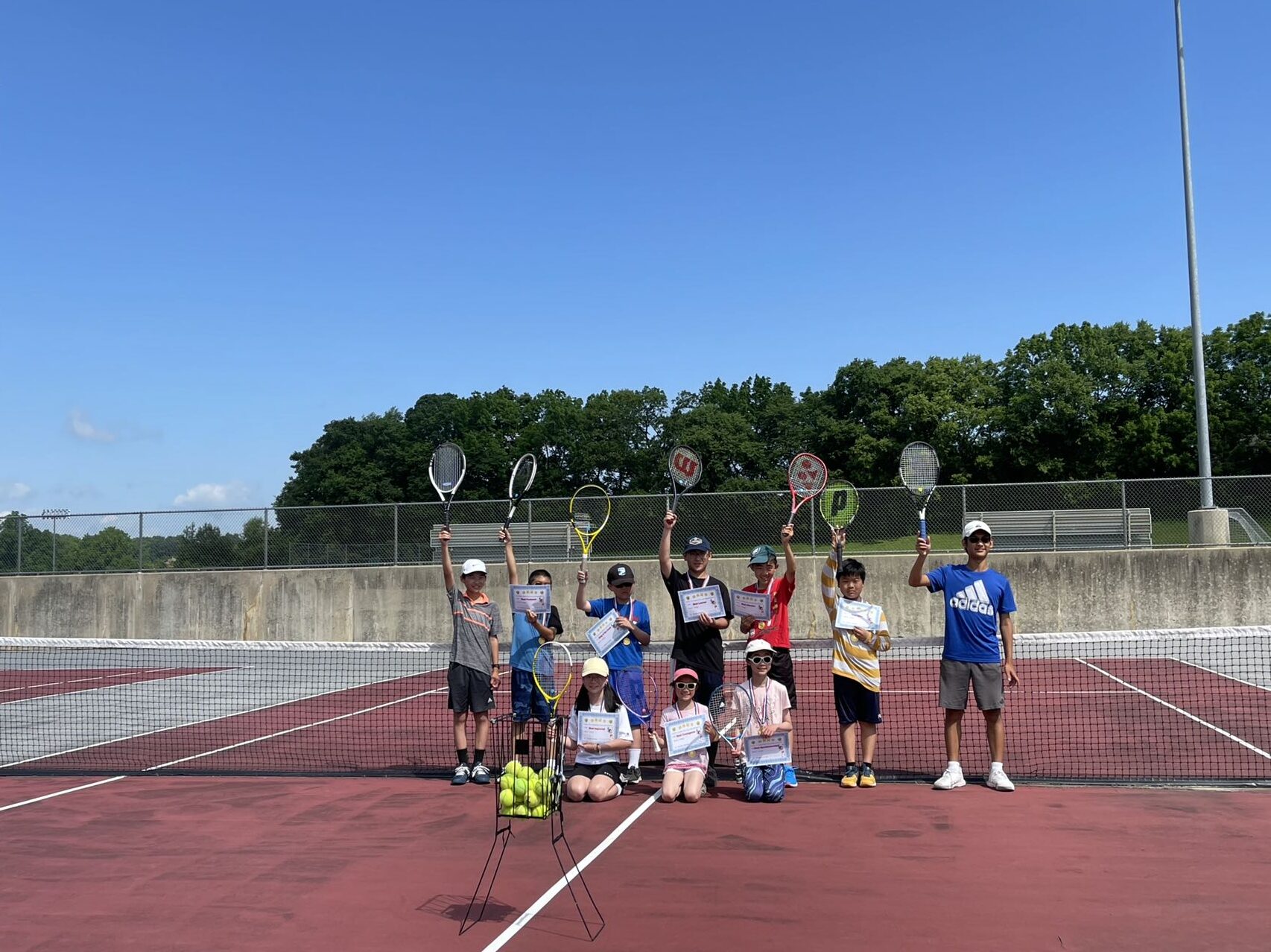2022 summer tennis camp players and coaches raising rackets and certificates