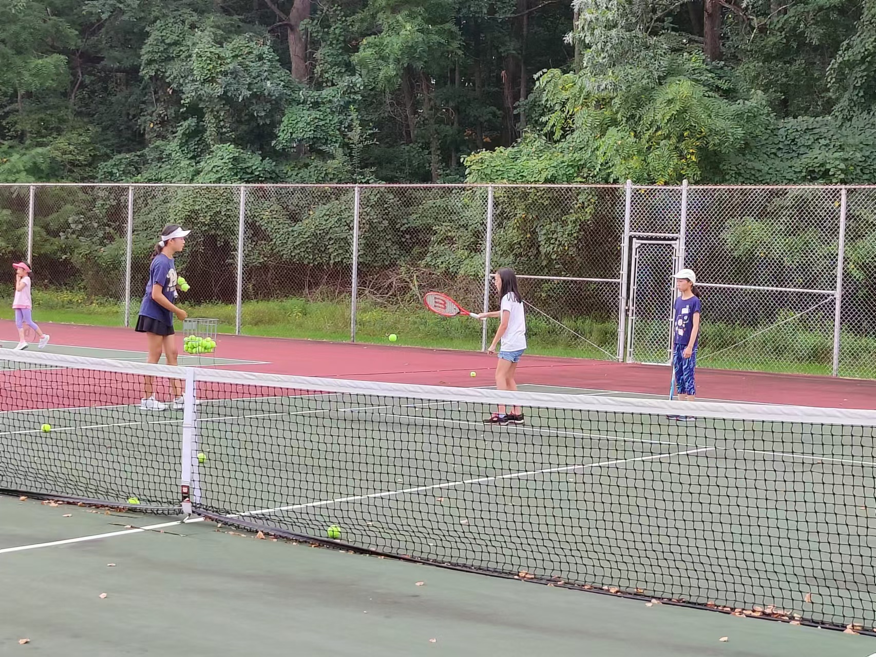A coach feeding tennis balls to young players during the fall club