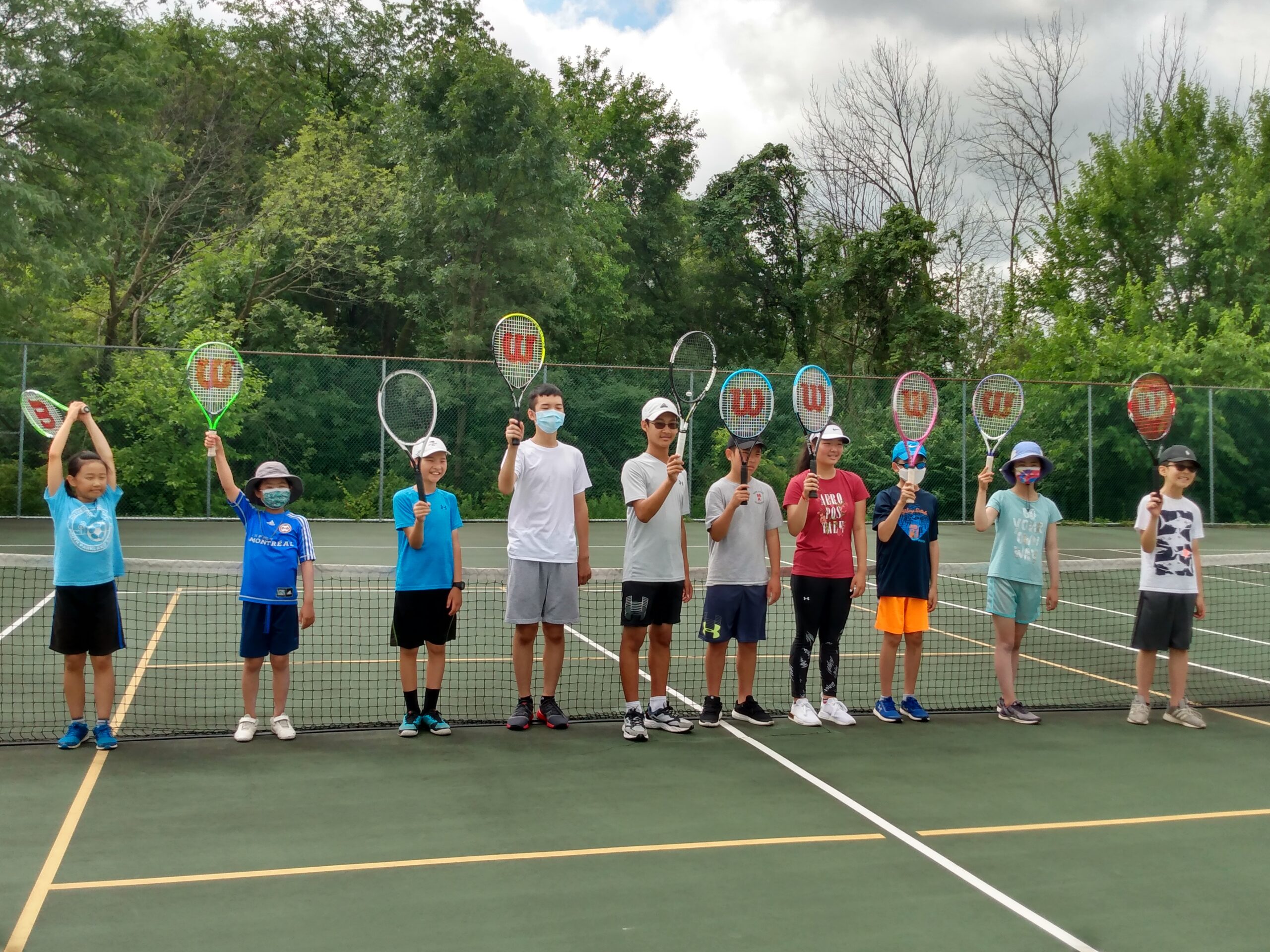 Players and coaches holding racquets together at the 2021 summer tennis camp